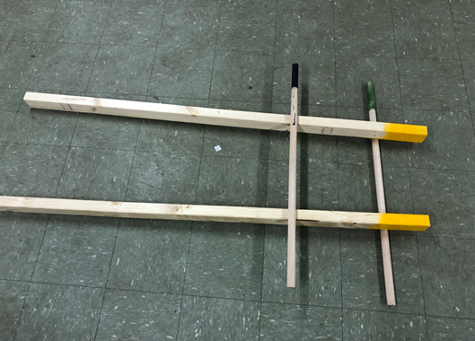 Place two yellow beams on the ground with a black stick over the beams and a green stick under